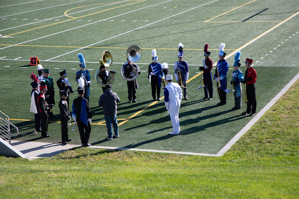 17 members of the all star brass band standing in a circle on the corner of a field.