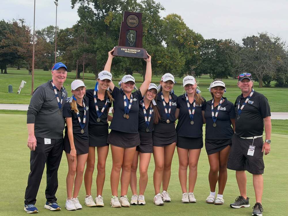 girls golf team posing for a photo and one athlete holds up a trophy