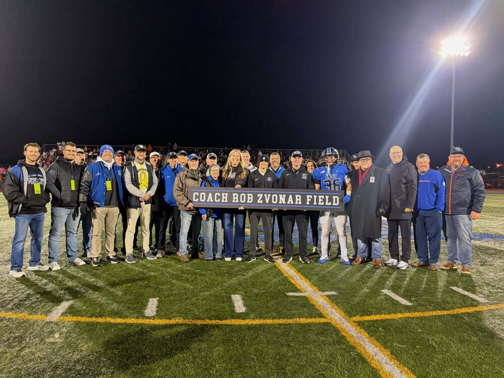 A group of people standing behind a sign that reads "Coach Rob Zvonar Field"