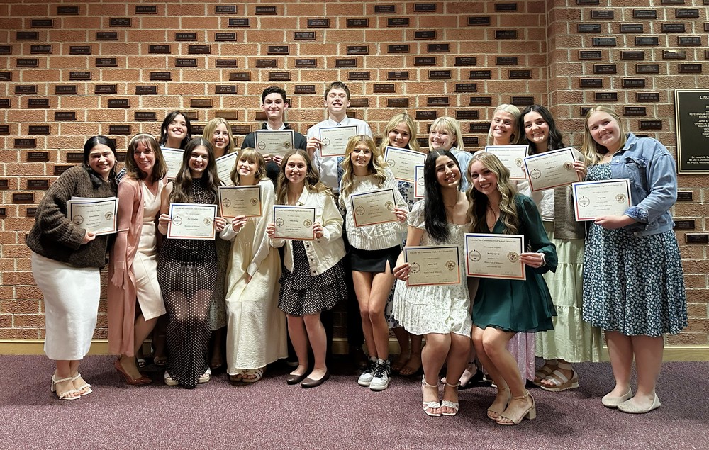 Students holding certificates standing in front of a brick wall, all smiling