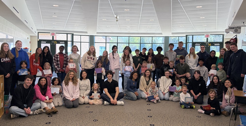 High school and kindergarten students stand in a semi-circle posing for a photo with their books