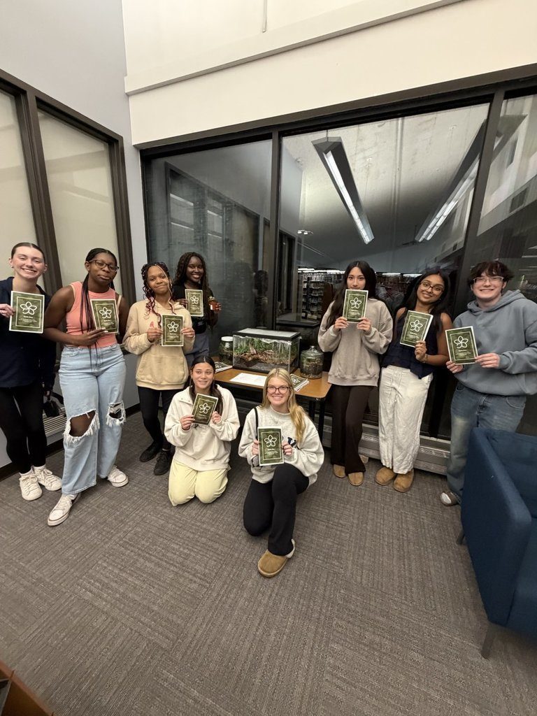 Nine students standing next to a terrarium, each holding a pamphlet 