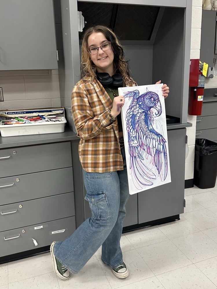 Student smiling holding a painting with art supplies in the background