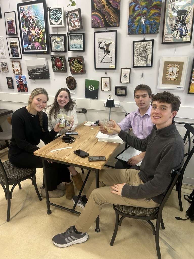 Four students sitting around a table cheersing their plastic coffee cups