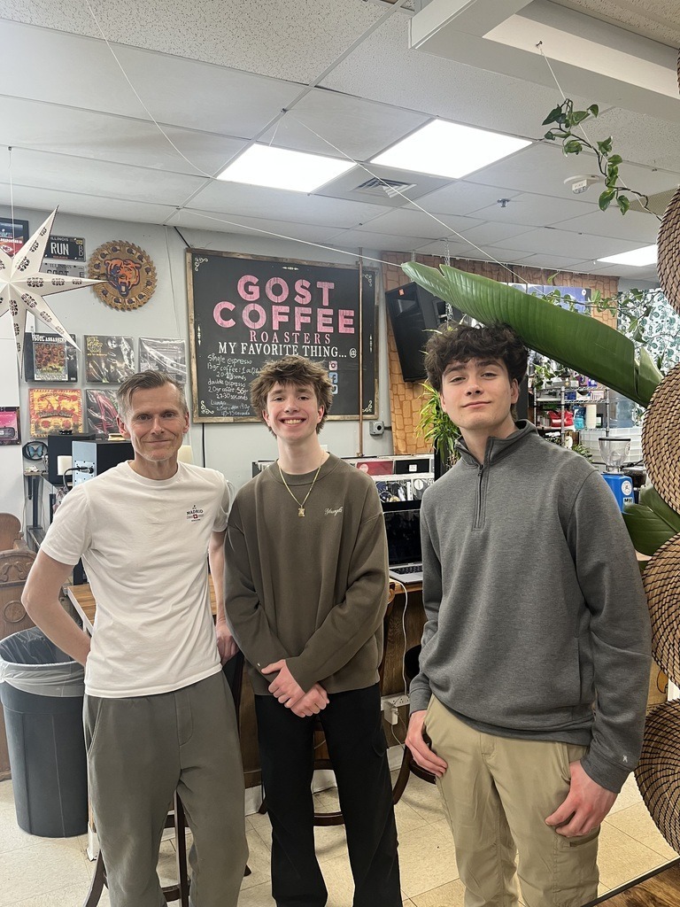 Two students posing with Daniel, owner of Gost Coffee, for a photo inside the shop