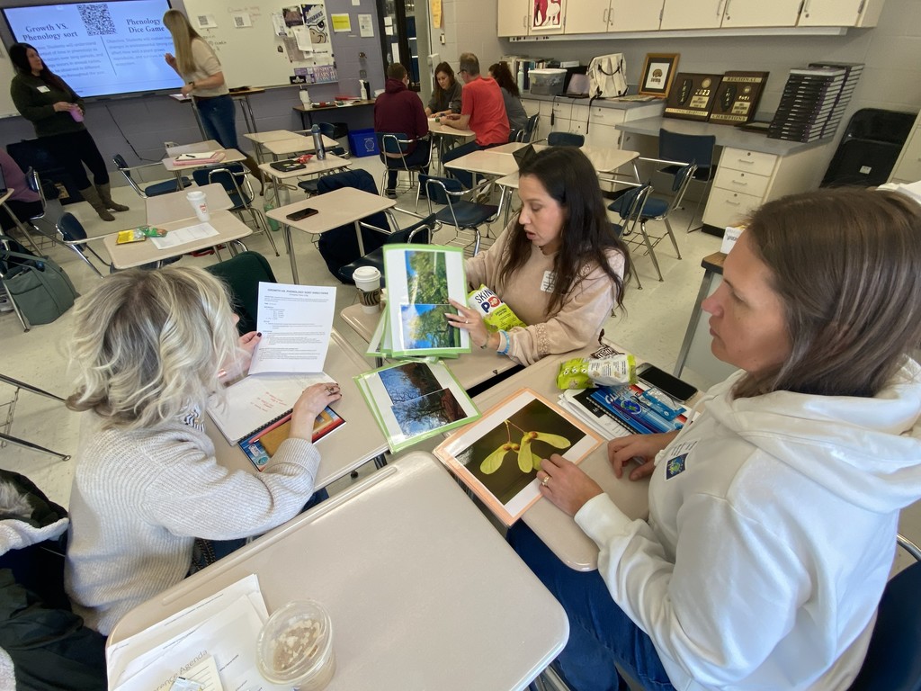 Three teachers looking at science materials sitting at classroom desks