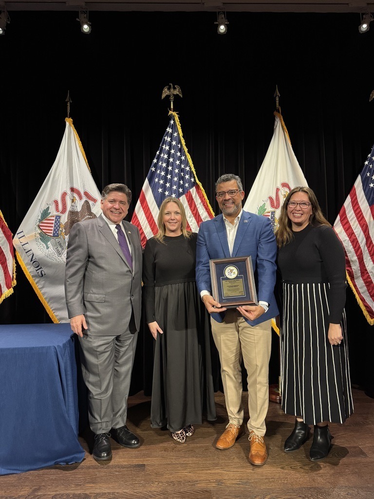 Governor Pritzker, Julie Flitcraft, Toriano Griggs, and Maria Wilson posing for a photo holding the Blue Ribbon plaque.