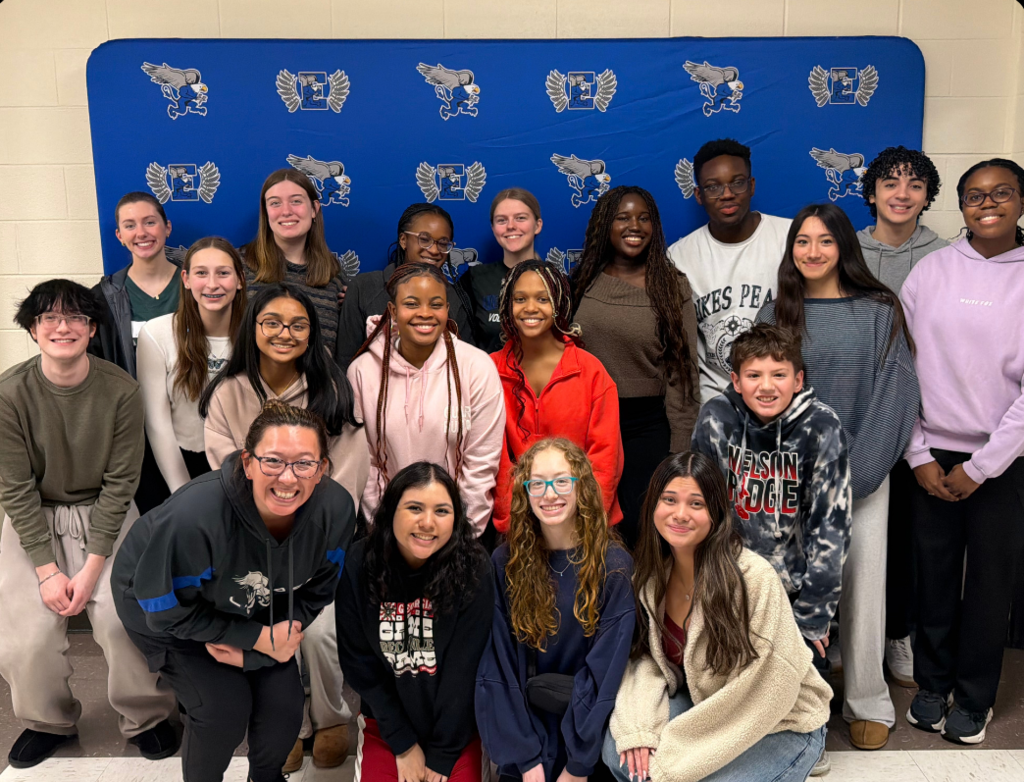 Group of students in casual attire posing for a photo in front of a blue backdrop.