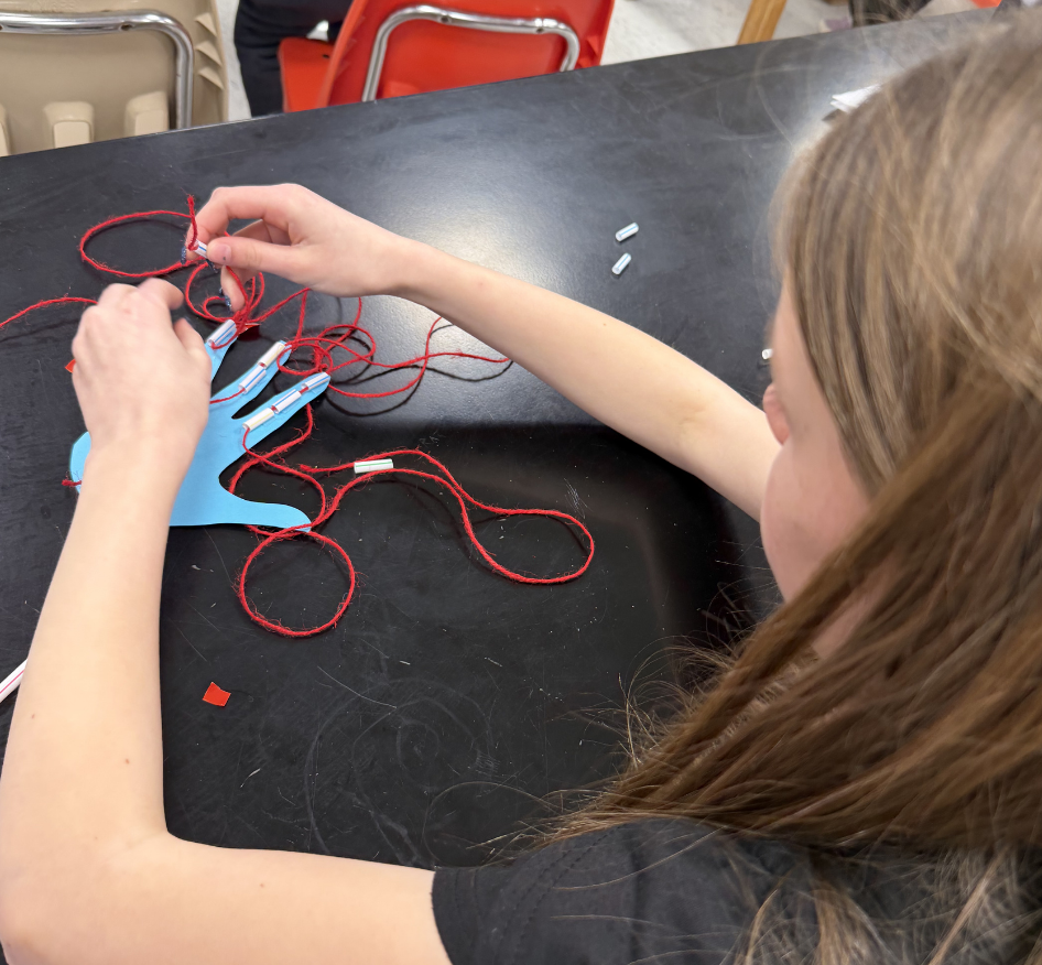 A person works on a craft project with blue gloves and red string on a table.
