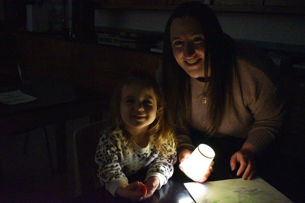 Woman and child sit at table in dim light. Child holds a constellation projector.