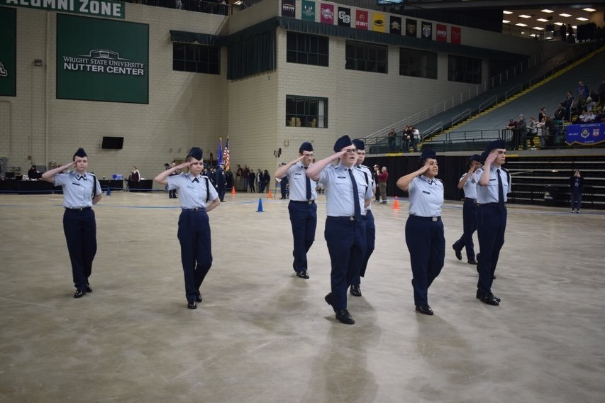 A group of people in uniform, possibly performing a ceremony, walk in a row on a concrete floor.