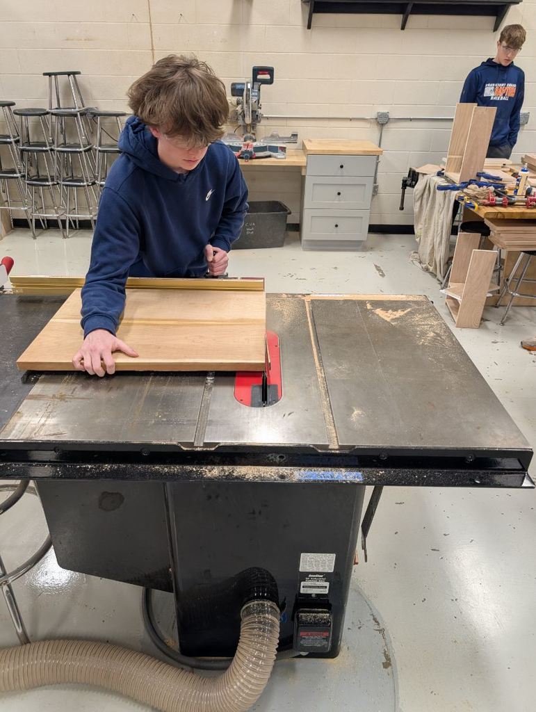 A person working on a table saw. A table saw sits on a table with a wooden board.