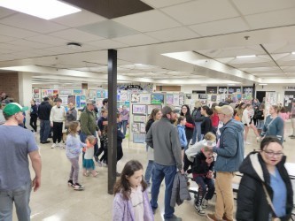 Indoor room with ceiling lights. Many people walking around, examining displays on the wall.