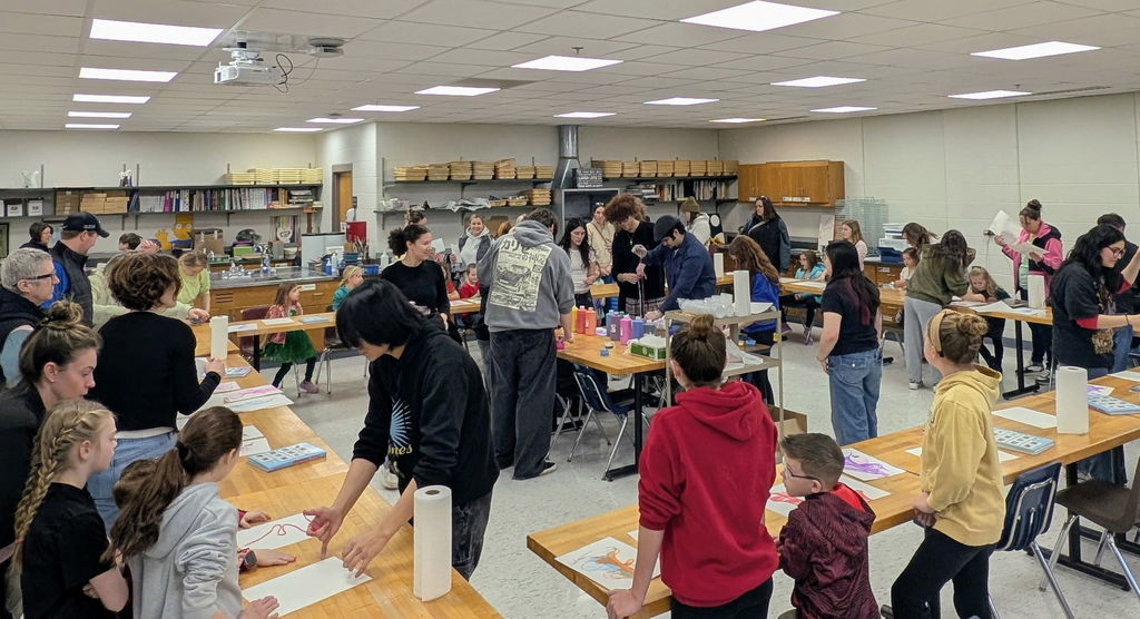 A room with white walls and tables where a group of people work on projects.