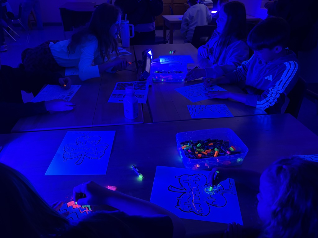 A group of people seated around tables with papers and art supplies, illuminated by blue light.