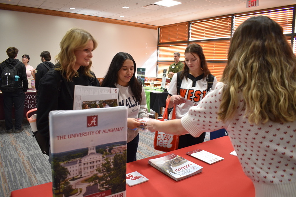 Four women stand around a table with brochures. One woman hands a brochure to another.