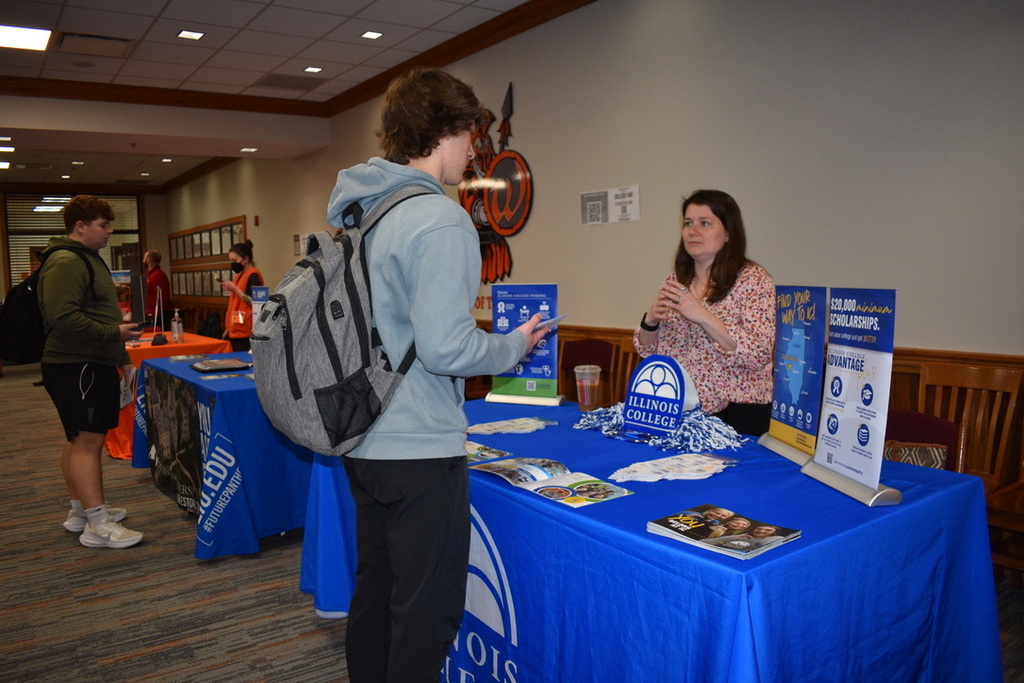 A student stands in front of a table speaking to a woman about Illinois College