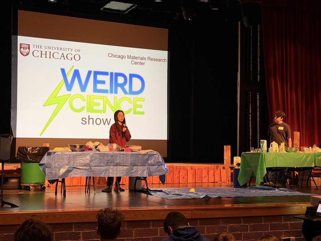 Two people on stage with tables, one speaking into a microphone, in front of a screen that says Weird Science.