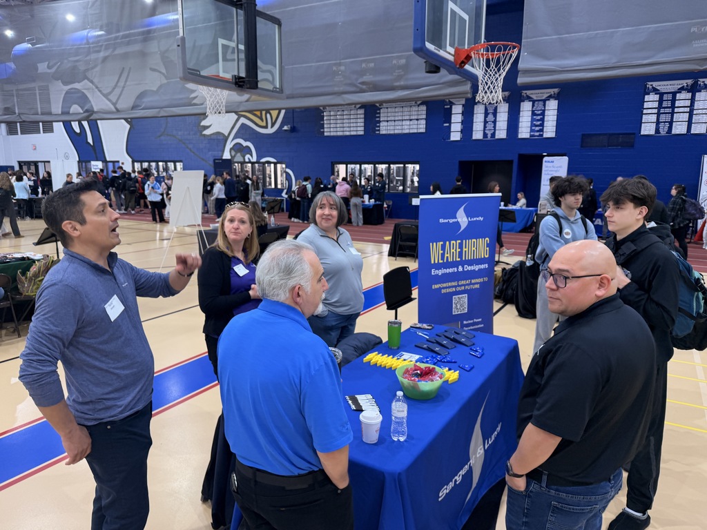 A group of people standing around a table in a gymnasium with a blue table and banner.