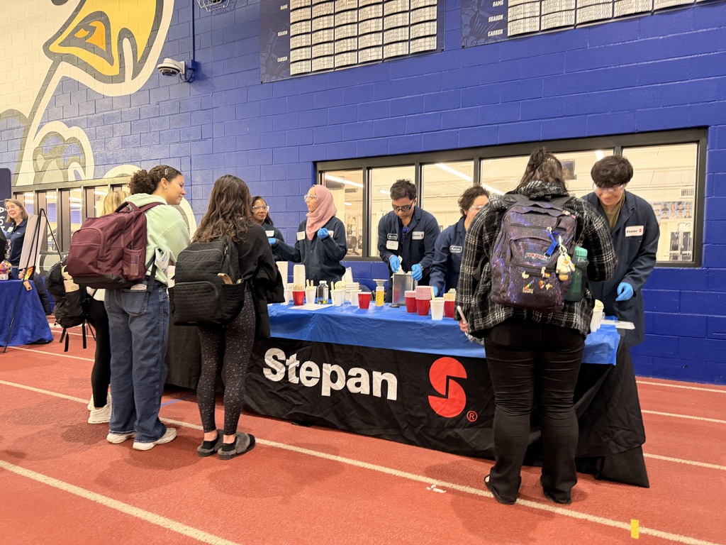 People in a sports hall, with a blue table in the foreground, labeled Stepan, surrounded by bottles.