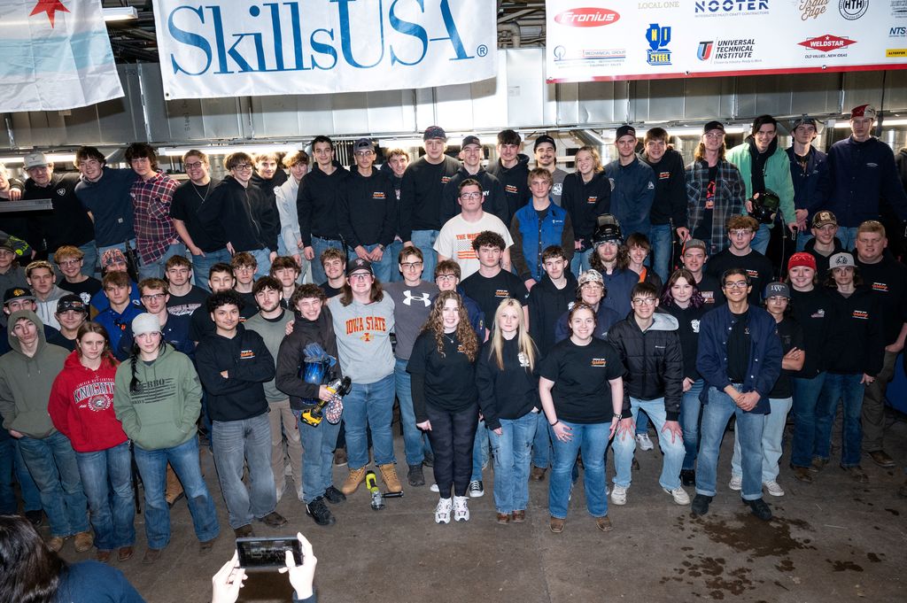 Large group of people wearing black and blue shirts standing together with a banner reading SkillsUSA above them.