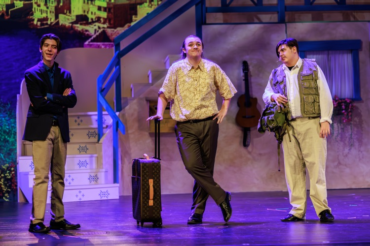 three students acting on stage with a suitcase