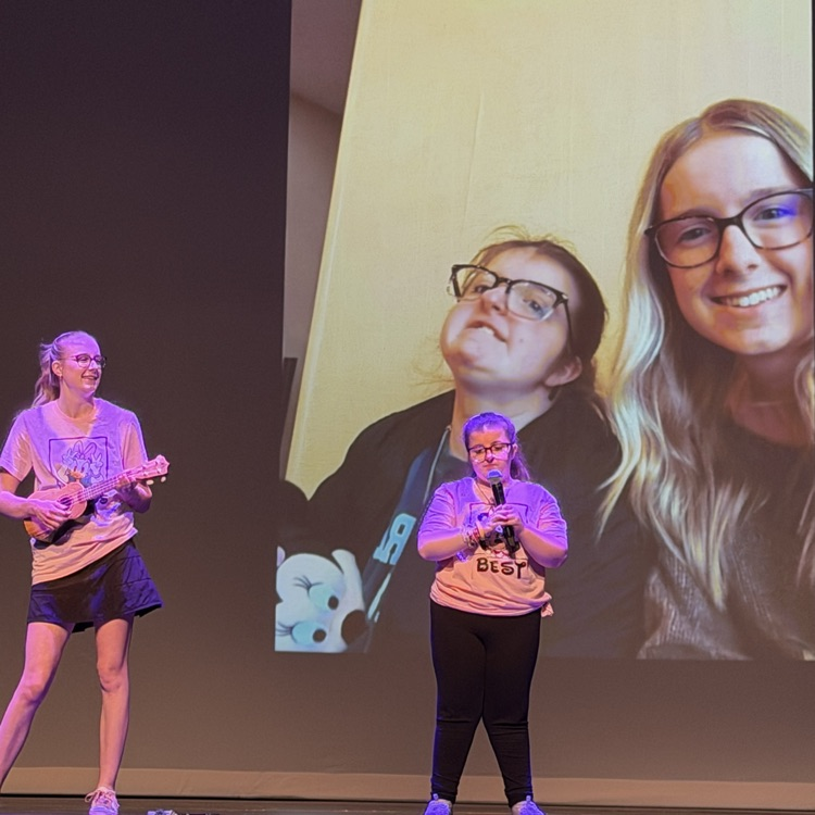 two students dancing on stage with photo of students in the background