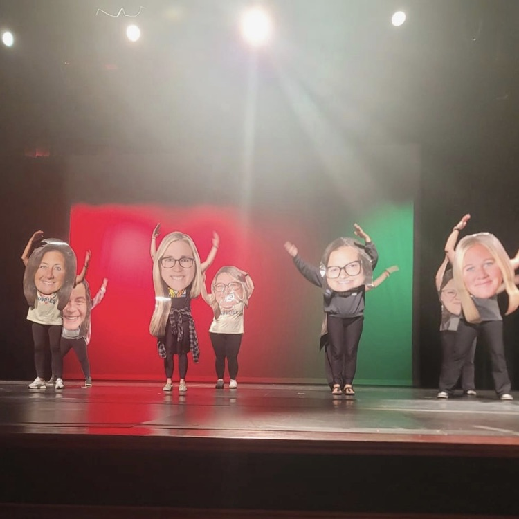 multiple staff dance on stage with posters of themselves