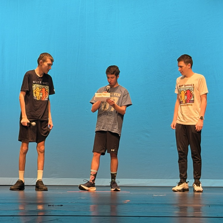 three students performing on stage with a teal background