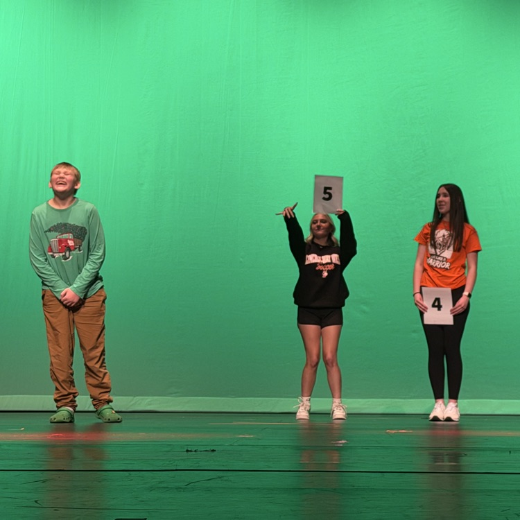 three students performing on stage with a green background