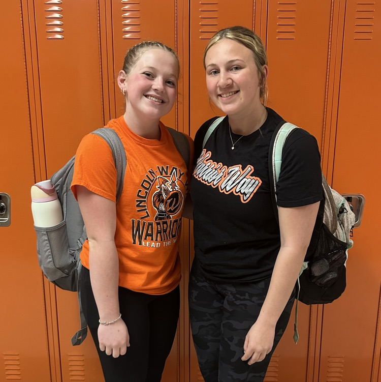 two students wearing orange in front orange lockers