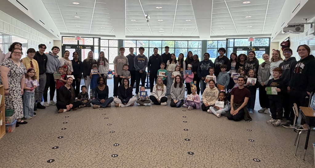 A large group of people gathered in a room, some seated on the floor, others standing, all smiling for a photo.