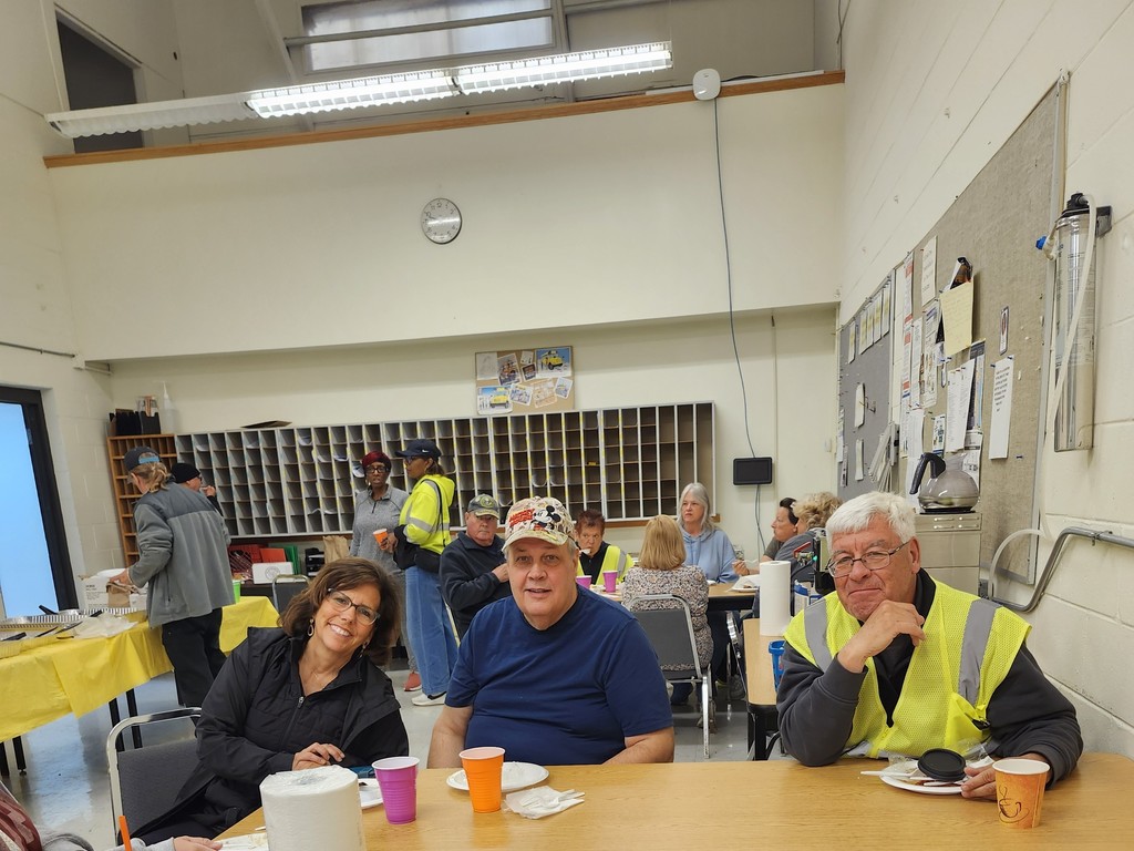 Bus driver appreciation breakfast, drivers sit at a table with food on plates and colorful cups, smiling