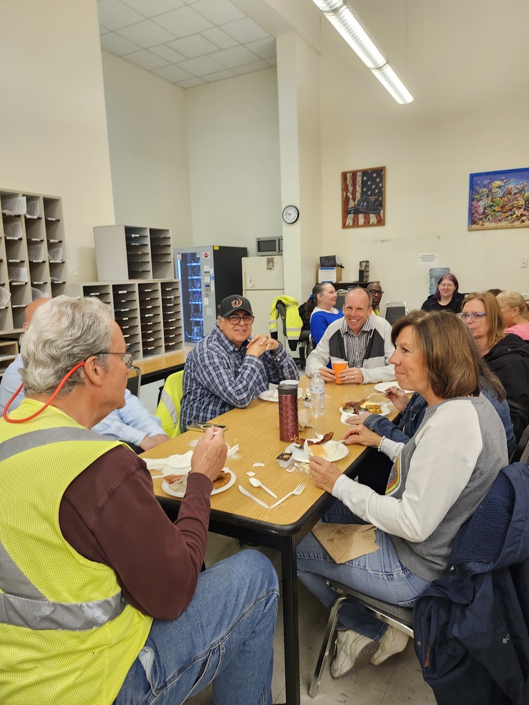 Bus driver appreciation breakfast, drivers sit at a table with food on plates and colorful cups, smiling