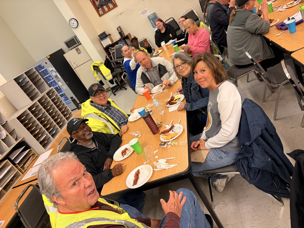 Bus driver appreciation breakfast, drivers sit at a table with food on plates and colorful cups, smiling