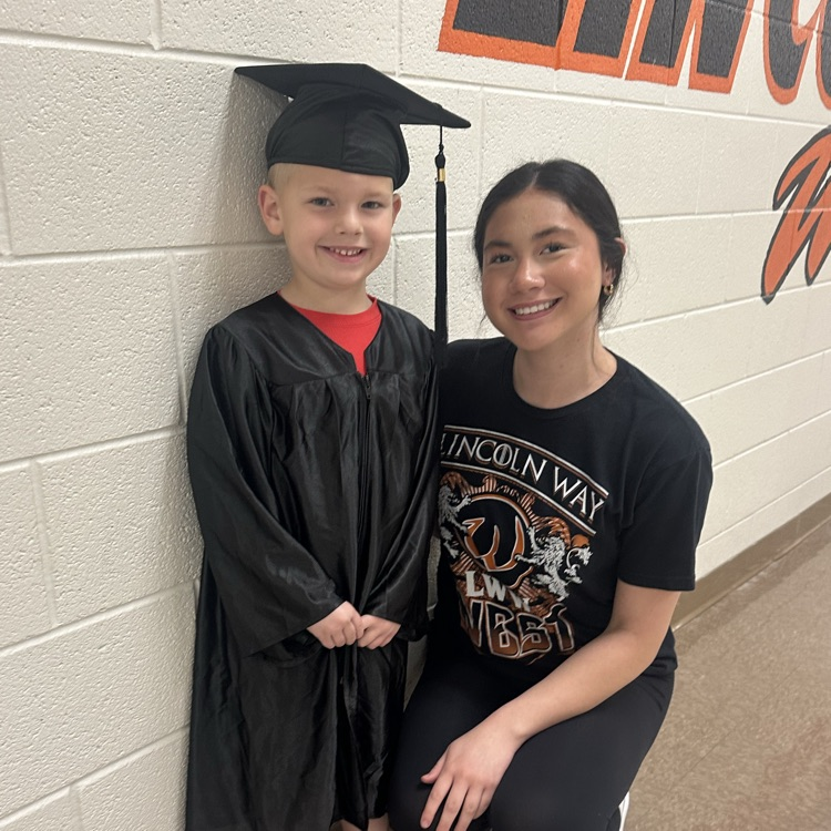 preschool student in graduation cap and gown with high school student in the hallway