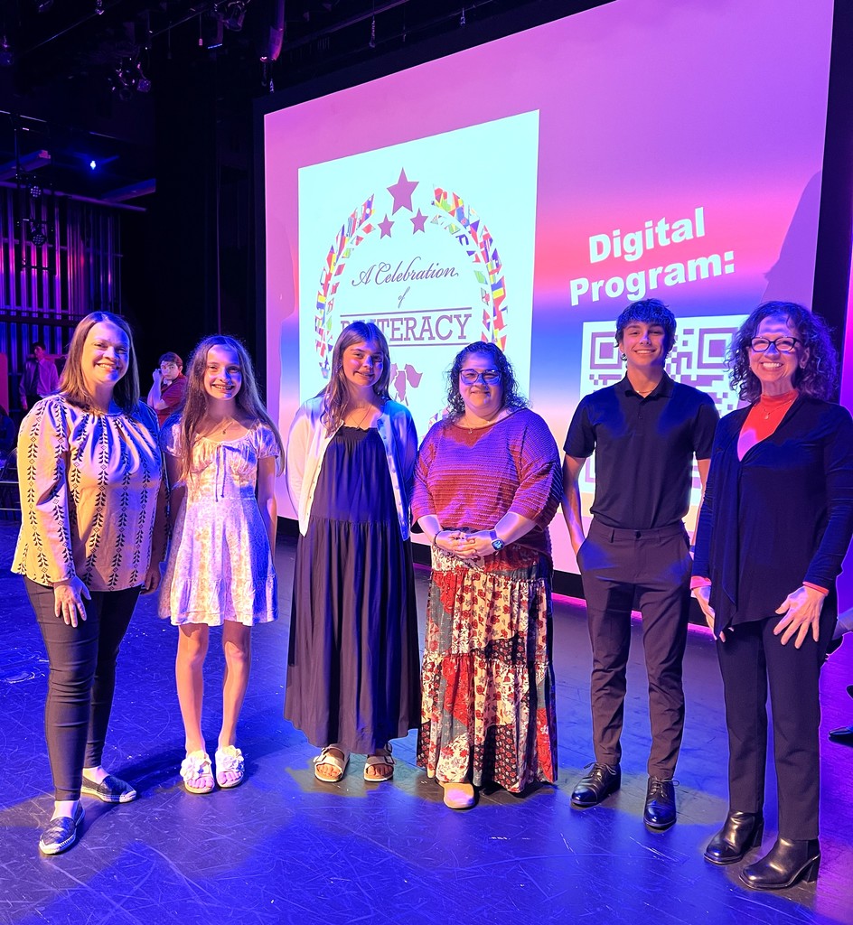 Students and staff stand on a stage, with a digital sign behind them reading "Digital Program."