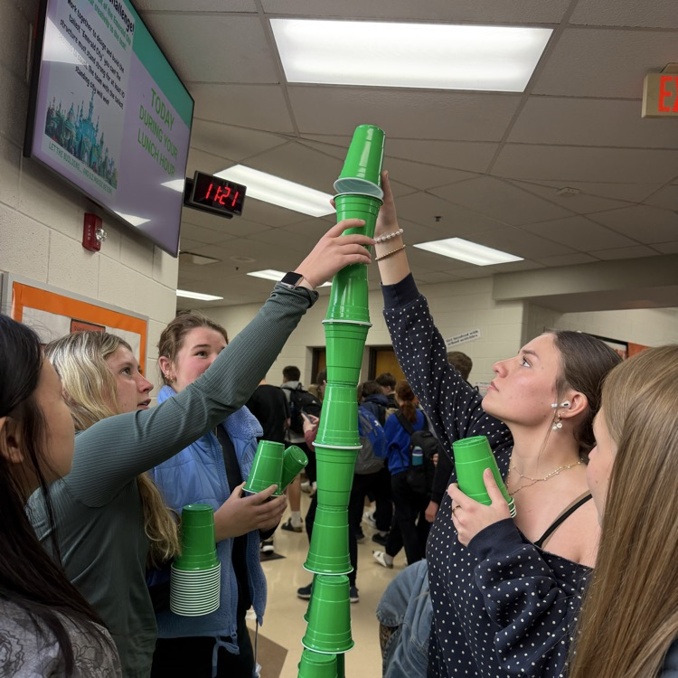 multiple students reaching up high to stack cups in a tower 