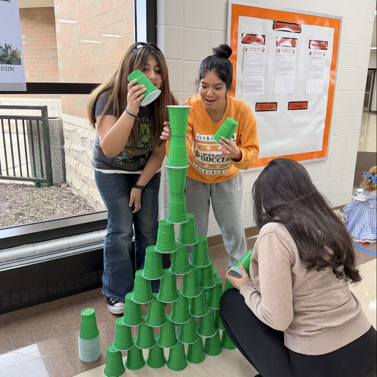 three students stacking a triangle shape of cups