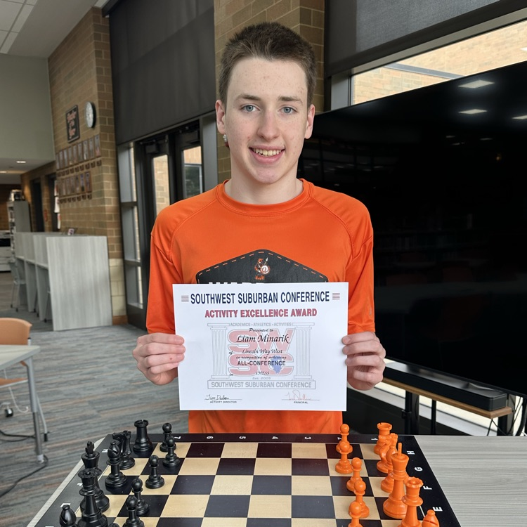 student holding certificate in front of chess board