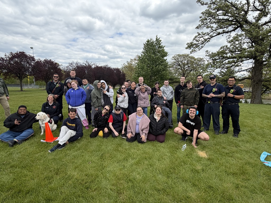 A group of people, including law enforcement, poses for a photo on a grassy field with trees.