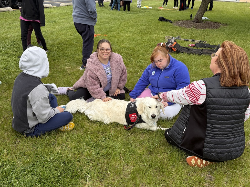 Four people sit around a dog on grass; one holds a leash. 