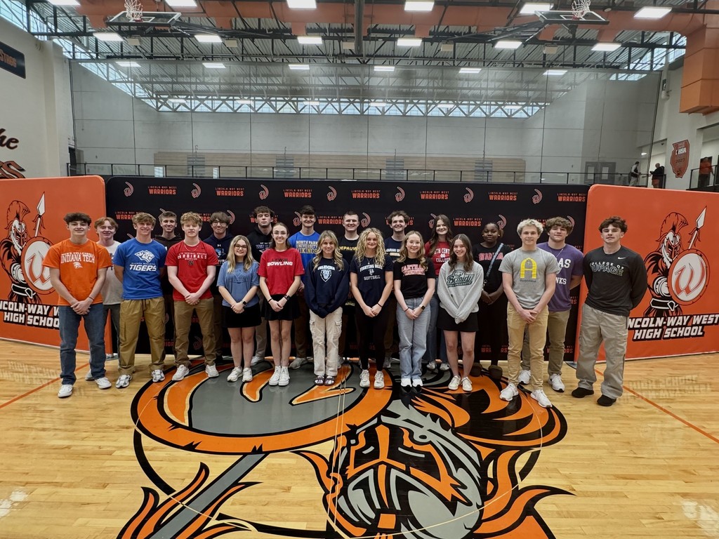A group of students stands in a line on a basketball court, with a school logo on the floor.