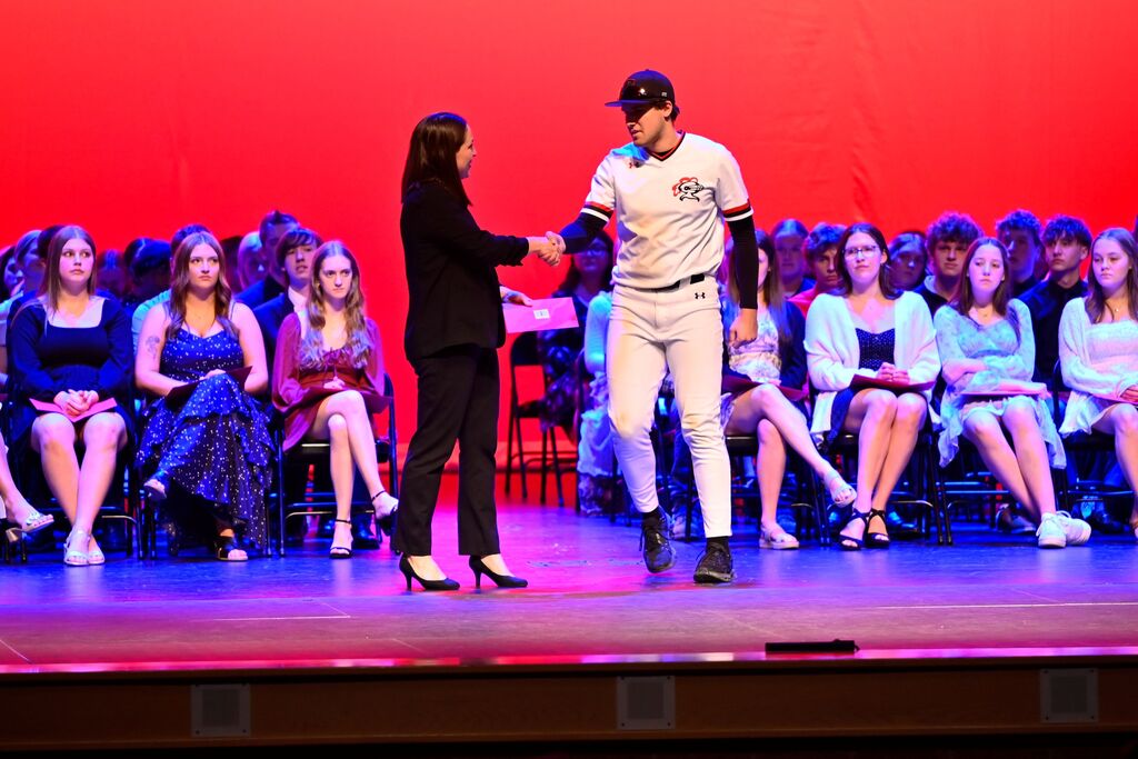 A person on stage shaking hands with a baseball player in front of an audience.