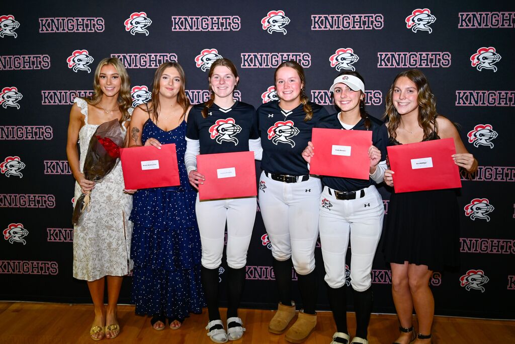 Six people pose for a photo in front of a wall displaying a team logo and the word "Knights".