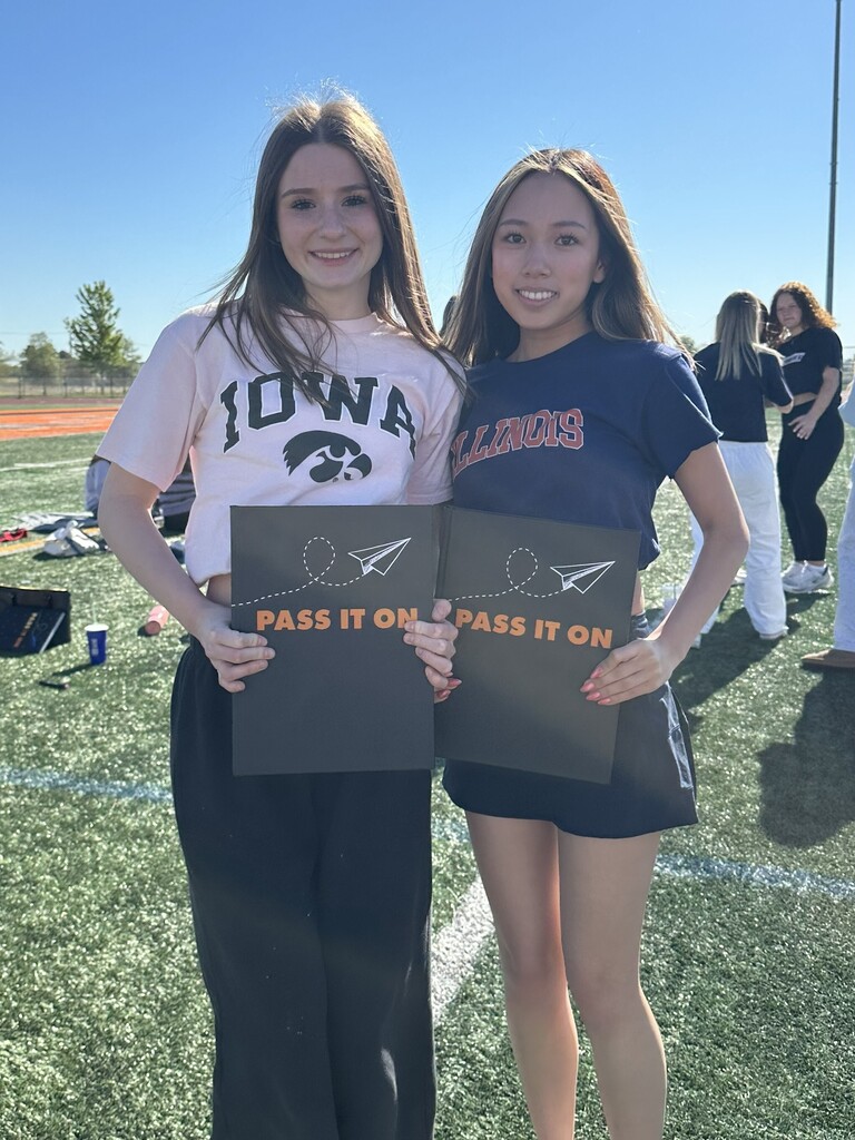 Two students stand on a field holding yearbooks
