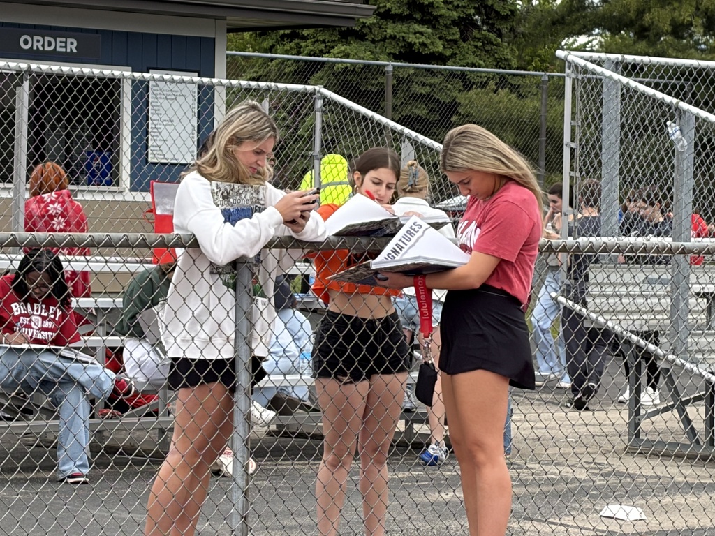 People stand behind a fence signing yearbooks