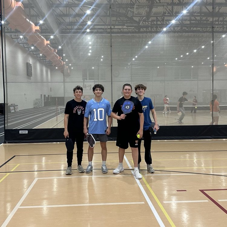 four students posing in the middle of a pickleball match