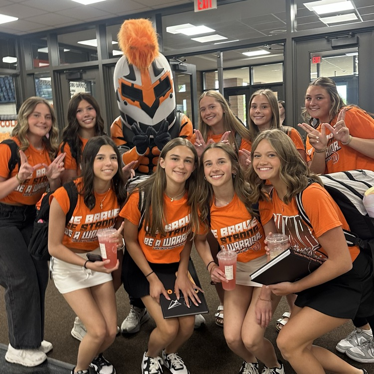 students wearing orange and posing for a picture with the Warrior
