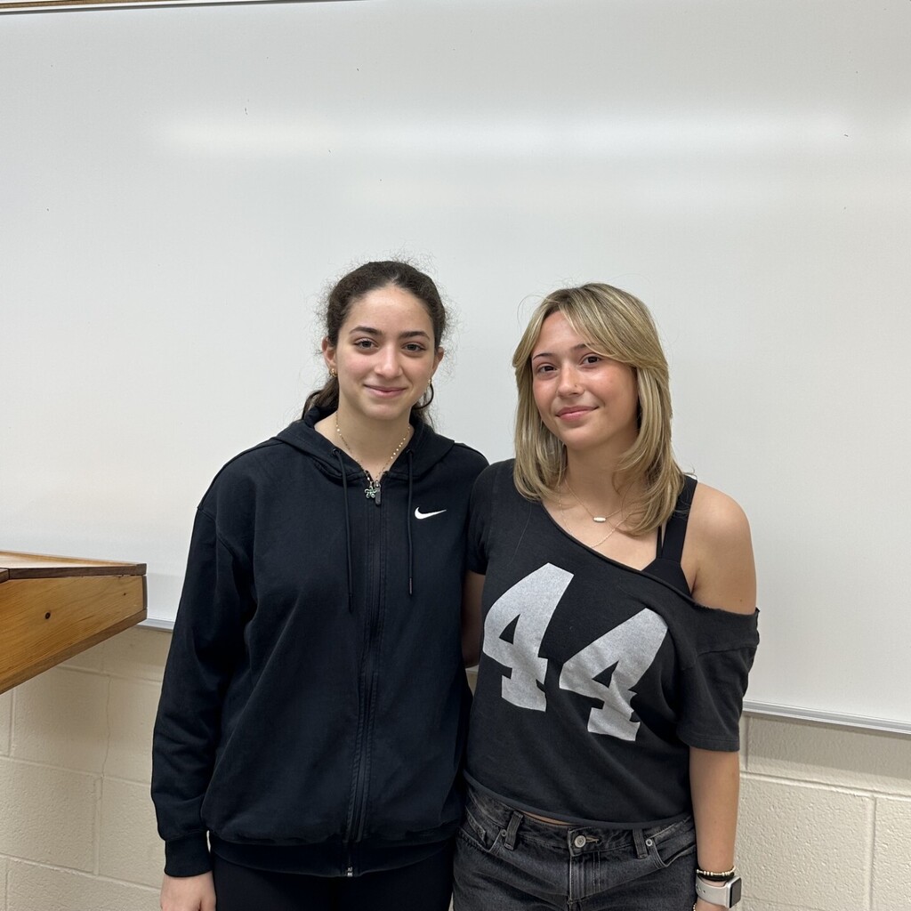 Two students posing next to a whiteboard. One wears a black hoodie and the other a black top with the number 44.